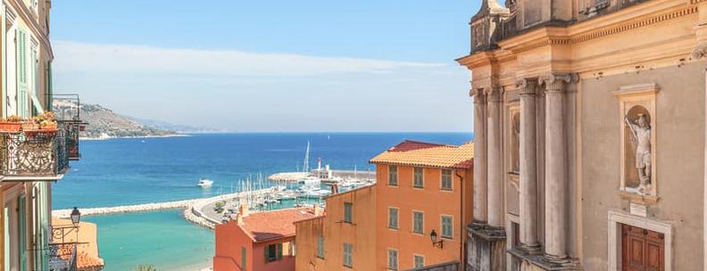 Strassengasse zwischen alter Kirche und bunten Häusern mit Blick auf das Mittelmeer in Menton, Frankreich.